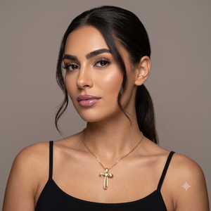 A realistic professional studio portrait photograph of a beautiful young woman with warm medium olive skin tone, sharp defined facial features, and a subtle confident expression, captured in a clean minimalist setting. She has thick perfectly shaped dark eyebrows, long voluminous lashes, almond-shaped deep brown eyes gazing slightly to her left, a straight nose, and full lips with a glossy soft mauve-pink finish. Her dark brown hair is pulled back into a sleek low ponytail with a few soft wavy strands framing the left side of her face and temple. She wears a uploaded necklace that sits gracefully along her collarbones, Her shoulders and upper chest are visible, dressed in a simple black spaghetti-strap camisole against a seamless neutral taupe-gray studio backdrop. Soft diffused studio lighting from the front-left creates gentle highlights on her cheekbones, forehead, and nose bridge while producing smooth skin texture with natural sheen and very subtle shadows under the jawline. The image is shot on a full-frame mirrorless camera with an 85mm f/1.4 lens at f/2.2, producing razor-sharp focus on the eyes and facial details, creamy shallow depth of field, and smooth bokeh in the background. Natural color grading with warm undertones, clean skin retouching, and high-resolution clarity in a polished editorial style. Output image quality must be exactly 2000 x 2000 pixels.